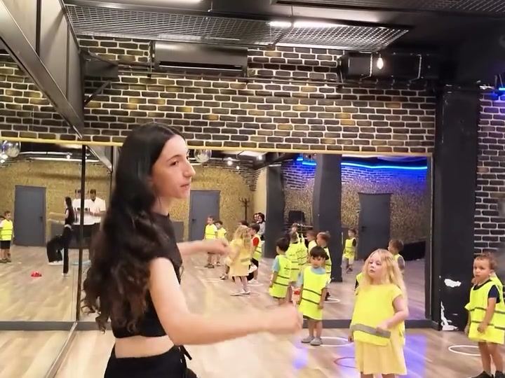 Öğretmen eşliğinde salonda hareket ve dans etkinliği yapan sarı yelekli çocuklar