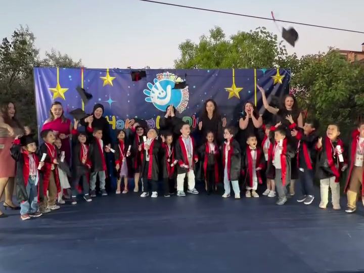 Kep ve cüppeleriyle sahnede sıralanmış mezun çocuklar
